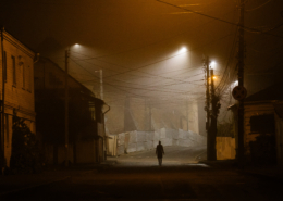 Lonely woman walking in foggy old city with street lights in a coat